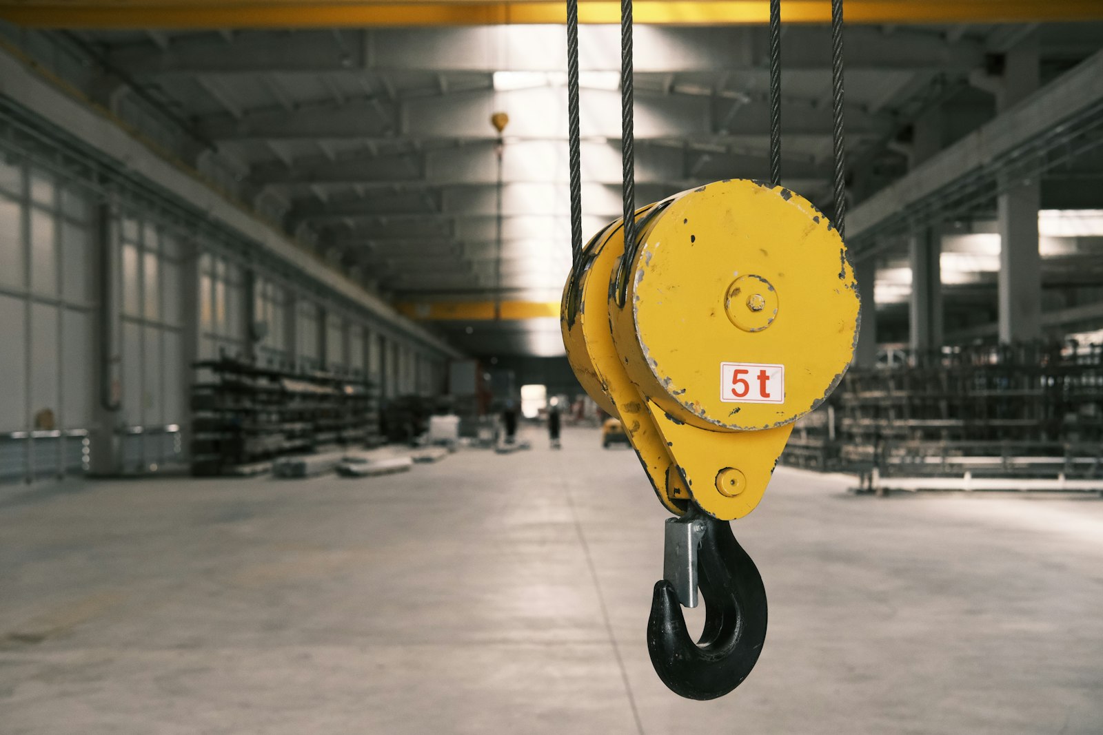 Yellow overhead crane hook block hanging in a warehouse bay
